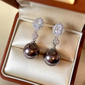 Close-up of elegant drop earrings featuring oval zircons and large dark pearls in a box