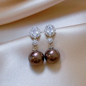 Detailed macro view of elegant silver needle earrings featuring oval zircon and lustrous brown pearls