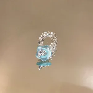 Close-up detail of a clear glass beaded ring featuring a light blue resin flower charm