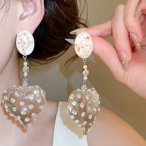 Detail showing transparent resin heart earrings with rhinestones and white flake studs