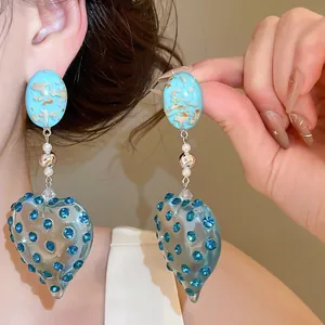 Close-up of unique heart-shaped resin earrings featuring sparkling blue rhinestone accents