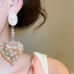 Close-up detail of a large heart-shaped resin earring featuring sparkling rhinestones