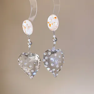 Detail showing clear resin heart earrings with sparkling rhinestones and speckled oval studs.