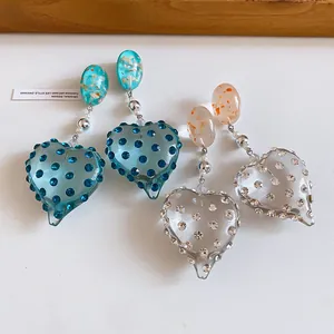 Close-up of handmade resin heart earrings with rhinestones in blue and clear.