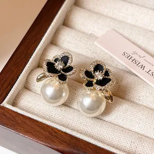 Vue détaillée de boucles d'oreilles camélia noir avec zircons et perle blanche pendante.