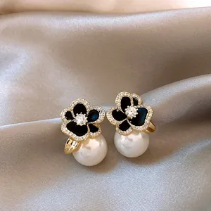Gros plan détaillé de boucles d'oreilles camélia noires avec zircon et perles blanches