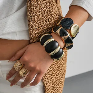 Vue détaillée de bracelets volumineux en acrylique noir et or sur le poignet d'un mannequin femme