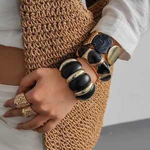 Gros plan sur des bracelets épais en acrylique noir et métal doré avec bagues