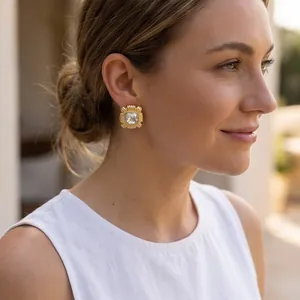 Detail of 18k gold-plated square stud earrings with textured frame and crystal stone