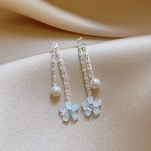Close-up detail of elegant long tassel earrings featuring light blue flowers and pearls