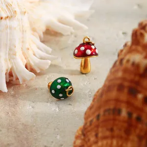 Detail shot of red and green enamel mushroom charms on a sandy beach with shells.