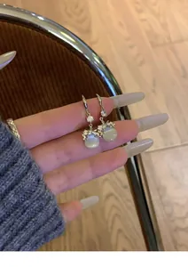 Detailed shot of elegant silver rhinestone and cat-eye stone drop earrings held by hand