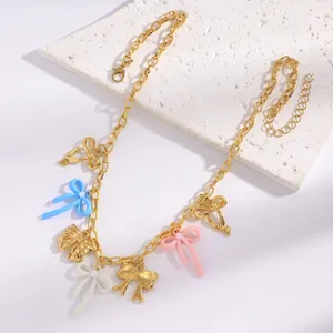 Detail shot of a gold chain necklace with colorful resin bow charms in pink and blue