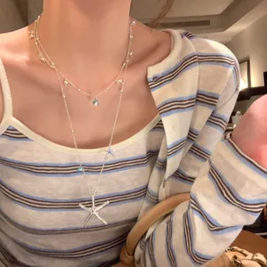 Detail view of a double-layered starfish and pearl necklace worn on a striped shirt.