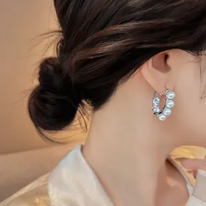 Close-up detail of C-shaped pearl earrings with sparkling rhinestones worn by model