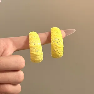 Primer plano detallado de pendientes de aro en C con encaje amarillo puestos en un dedo.