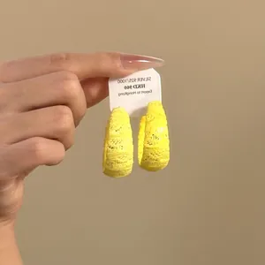 Vista detallada de unos aretes de aro de encaje amarillo sostenidos por una mano