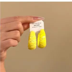 Detalle de pendientes de aro en forma de C amarillos con textura de encaje vibrante