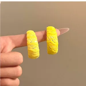 Primer plano detallado de aretes de aro amarillos envueltos en encaje mostrados en un dedo