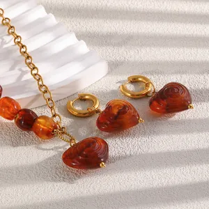 Close-up detail of retro 18K gold plated chain necklace and amber acrylic heart earrings