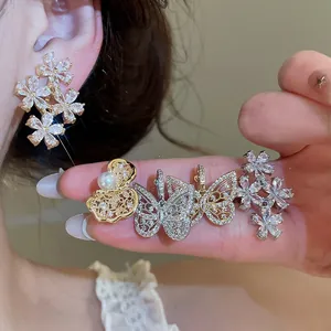 Close-up detail of sparkling zircon flower and butterfly ear clips on woman fingers and ear