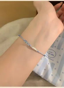 Hand wearing a minimalist blue woven bracelet with silver fish charm and small beads