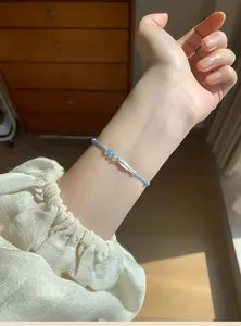 Close-up of a blue braided string bracelet featuring a dainty silver fish charm.