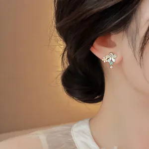 Close-up of a delicate floral stud earring with cat-eye stones and rhinestones worn on ear