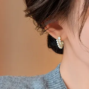 Élégantes boucles d'oreilles en C avec perles blanches et zircons portées sur l'oreille