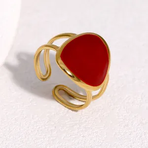 Close-up detail of a minimalist gold-plated stainless steel ring featuring red enamel.
