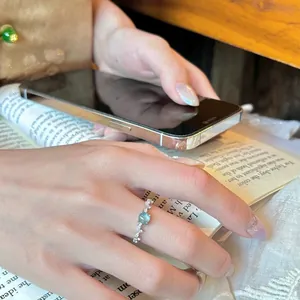 Primer plano detallado de un elegante anillo plateado con circón verde redondo al dedo.