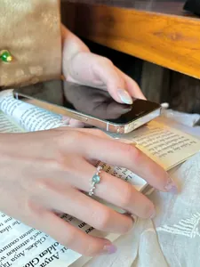 Primer plano detallado de un anillo de plata con circonitas y una piedra verde en un dedo.
