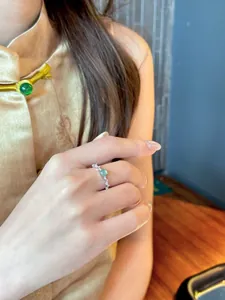 Primer plano de un anillo abierto plateado con circón verde en el dedo de una modelo.