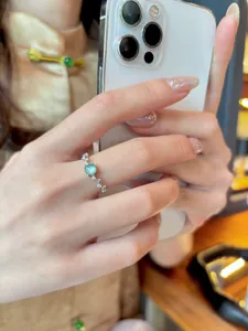 Primer plano de un elegante anillo abierto de circón en el dedo índice sujetando un móvil blanco