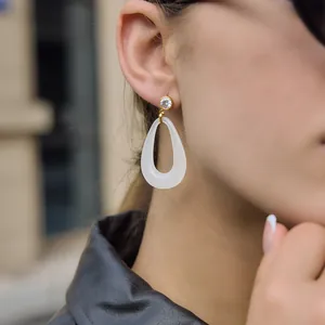 Close-up view of elegant white resin teardrop dangle earrings worn by a model in natural light