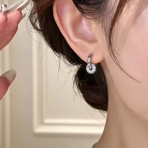 Close-up of silver hoop earring with crystal-set disk pendant on ear