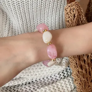 Nahaufnahme eines rosa-weißen marmorierten Acrylperlen-Armbands am Handgelenk.