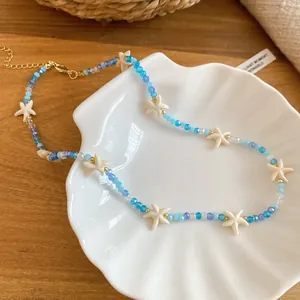 Detail van zomerse zeester kralenketting met blauwe kristallen kralen op een schelpenbord