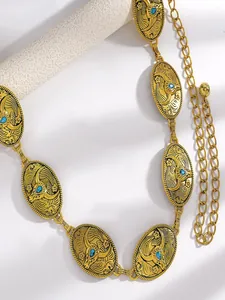 Gros plan d'une chaîne de taille dorée vintage avec gravures et strass bleus.