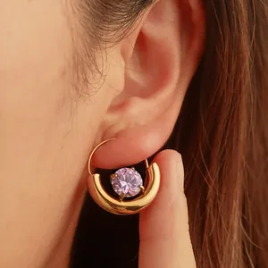 Nahaufnahme eines goldenen geometrischen Ohrrings mit lila Zirkon am Ohr.