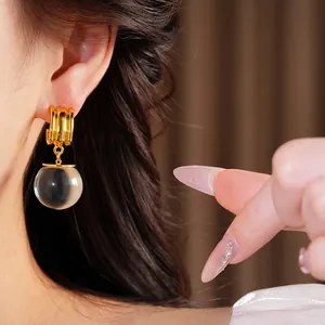 Boucles d'oreilles créoles dorées avec pendentif sphère en résine, portées par un modèle.