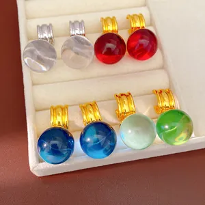 Gros plan de plusieurs boucles d'oreilles boules en résine colorée dans un plateau blanc