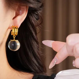 Détail d'une créole dorée avec une perle en résine transparente sur l'oreille d'un mannequin.