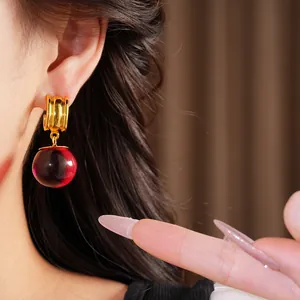 Détail de boucles d'oreilles créoles dorées avec une boule en résine rouge foncé