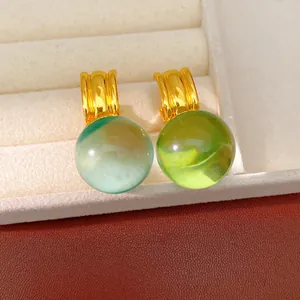 Gros plan de boucles d'oreilles boules en résine verte et menthe avec anneaux dorés en boîte