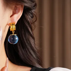 Gros plan de boucles d'oreilles dorées élégantes avec une sphère en résine bleu foncé