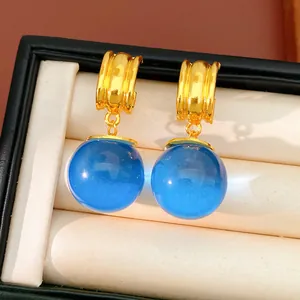 Détail macro de boucles d'oreilles dorées avec des sphères en résine bleue translucide