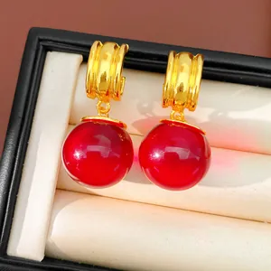 Gros plan de créoles dorées avec grands pendentifs boules en résine rouge dans une boîte