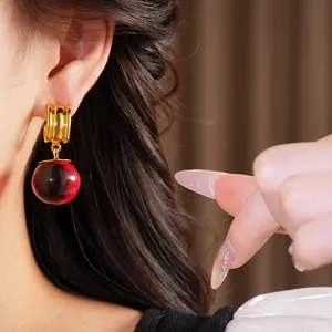 Gros plan de boucles d'oreilles créoles dorées avec goutte en résine rouge sur mannequin.