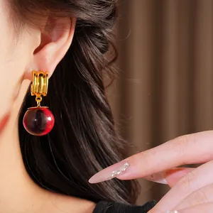 Vue détaillée de boucles d'oreilles dorées avec une goutte en résine rouge bordeaux